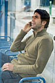 Junger Mann sitzt in einer Bushaltestelle und telefoniert mit dem Handy