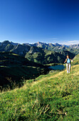Hiker above lake Seealpsee with view to Allgaeu range, Allgaeu, Swabia, Bavaria, Germany
