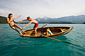 Young man pushes girlfriend from a rowing boat into turquoise water, Lake Faak, Carinthia, Austria