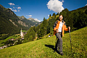 Woman hiking over alp above Heiligenblut with pilgrimage church Zum hl. Pluet, view to Grossglockner, Heiligenblut, Carinthia, Austria