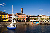 Sailling boat on Lake Maggiore, harbour promenade with spire of church Santi Pietro Paolo in background, Ascona, Ticino, Switzerland