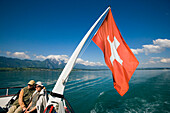 Couple sitting at stern of a ship, swiss flag blowing in the wind, Lake Thun, Bernese Oberland (highlands), Canton of Bern, Switzerland