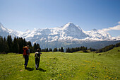 Two people hiking uphill at Bussalp (1800 m), view to Eiger North Face (3970 m), Grindelwald, Bernese Oberland (highlands), Canton of Bern, Switzerland