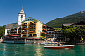 View over lake Wolfgangsee to parish and pilgrimage church and Hotel Im Weissen Rössel am Wolfgangsee, two people in a canoe passing, St. Wolfgang, Upper Austria, Salzkammergut, Austria