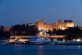 Ships and boats anchoring in Mandraki harbour (translated literally: fold) in the evening, illuminated Palace of the Grand Master and Nea Agora in background, Rhodes Town, Rhodes, Greece