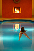 Frau schwimmt in einem Schwimmingpool, brennender Kamin im Hintergrund, Seehotel Neuklostersee, Nakenstorf, Mecklenburg-Vorpommern, Deutschland, MR, PR