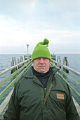 fisherman at the Baltic sea, Germany, portrait, people from germany, german, man with cap, man with pompom hat, pompom hat, green pompon hat, direct view, direct look in the camera, straight look in the camera, grim, a grimmer man, grimmer look, headgear,