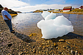 Ein Tourist betrachtet einen Eisklotz am Strand von Narsaq, Südgrönland