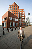 Young business man walking past Neuer Zollhof, modern architecture from Frank Gehry, Media Harbour, Düsseldorf, state capital of NRW, North-Rhine-Westphalia, Germany