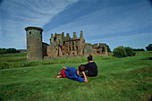 A couple looking at the ruins of Caerlaverock Castle, near Dumfries, Dumfries and Galloway, Scotland