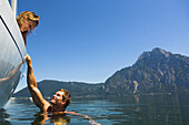 Man swimming in the water, Woman watching from a boat, sailing on Lake Traunsee, Upper Austria, Austria