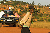 Two people looking at a map on the hood of a car in the background, a local woman crossing the road in the foreground, Madagascar, Africa