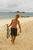 Man walking along the beach carrying a fish, Madagascar, Africa