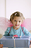 Mädchen (3-4 Jahre) mit Schmetterlingsflügeln hält ein Geschenk