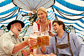 Couple and a mature man clinking beer glasses in a beer tent