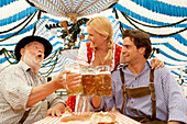 Couple and a mature man clinking beer glasses in a beer tent