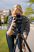 Junge Frau fotografiert mit einer Kamera auf einem Stativ, Luxemburg