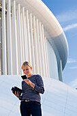 Young woman standing in front of Philharmonie and looking at a photo, Luxembourg, Luxembourg