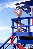 Rettungsschwimmer steht vor einem Rettungsschwimmerhäuschen am Strand, South Beach, Miami, Florida, USA