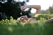 Young woman lying on grass smelling flower, Icking, Bavaria, Germany