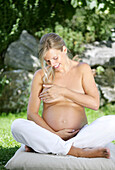 Topless pregnant woman sitting in garden, Styria, Austria
