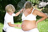 Boy (4-5 years) drawing circle on pregnant woman's belly, Styria, Austria