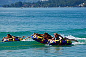 three young women tube riding behind motor boat, lake Abersee, lake Wolfgangsee, Salzkammergut, Salzburg, Austria