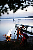 Zwei Kinder stehen rund ums Feuer, abenddämmerung, Worthsee, Oberbayern, Bayern, Deutschland