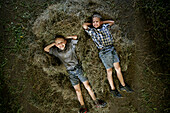 Two boys (8-9 years) lying on haystack, Walchstadt, Upper Bavaria, Bavaria, Germany, MR