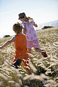 Boy and girl running through meadow of shore grass, Sysne, Gotland, Sweden