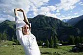 Frau streckt sich vor Gebirgspanorama, Heiligenblut, Nationalpark Hohe Tauern, Kärnten, Österreich