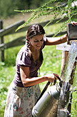 Frau füllt Milchkanne an einem Gebirgsbach, Heiligenblut, Nationalpark Hohe Tauern, Kärnten, Österreich