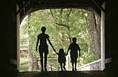 Silhouette of mom with two children in covered bridge. Pennsylvania, USA