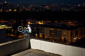 Trialbiker auf Kante von Hochhaus, Linz, Abend
