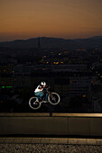 Trialbiker auf Kante von Hochhaus, Linz, Abend