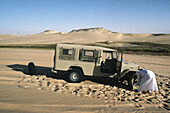 Tuareg changing flat tyre of his 4 wheels drive. Djanet oasis, Sahara desert. Algeria