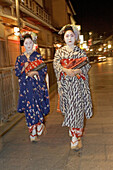 Two Maiko (geisha apprentices) walking to their evening appointment in the traditional quarter of Gion . Kyoto. Kansai, Japan (Model Release)