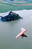 Microlight aircraft flying above Mont St. Michel at high tide. Normandy, France