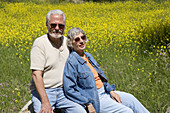 Portrait of active senior couple having a relaxing moment sitting in front of a field of yellow flowers.