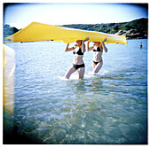 Girls holding a yellow canoe at the beach