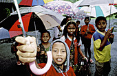 Children holding umbrellas for tourists visiting Baths site. Tampaksiring. Bali Island. Indonesia