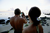 Couple taking digital photos on the beach. Hotel Resort Oberoi. Pointe Aux Piments. Mauritius