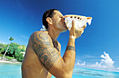 Tattoed young man blowing in a seashell. Bora Bora, Leeward Islands. French Polynesia