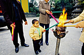 Ritual of burning incense sticks at temple, adults and child. Hangzhou. Zhejiang province, China