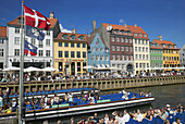 Flags, tour boats, ancient houses and waterfront cafe terraces at Nyhavn ( New Harbor ), Copenhagen. Denmark