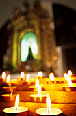 Opferlichter und Altar mit Marienbild unscharf im Hintergrund, Chiesa di San Stefano, Belluno, Italien