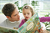 Father and daughter (3-4 years) reading a book, Munich, Germany