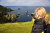 A woman filming the wild coast of Hermaness, Nature Protection Area, island of Unst, Shetland islands, Scotland, Great Britain, UK