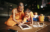 Wat Prok. Burmese refugee monk teaching child to write. Bangkok. Thailand.