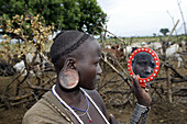 Mursi woman looking herself on a mirror. Omo valley. South Ethiopia.